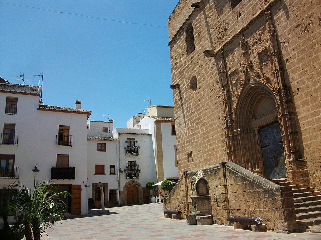 Plaça de l'Església in the old town — the sandstone flank of Sant Bartomeu on one side, whitewashed houses with wrought-iron balconies on the other